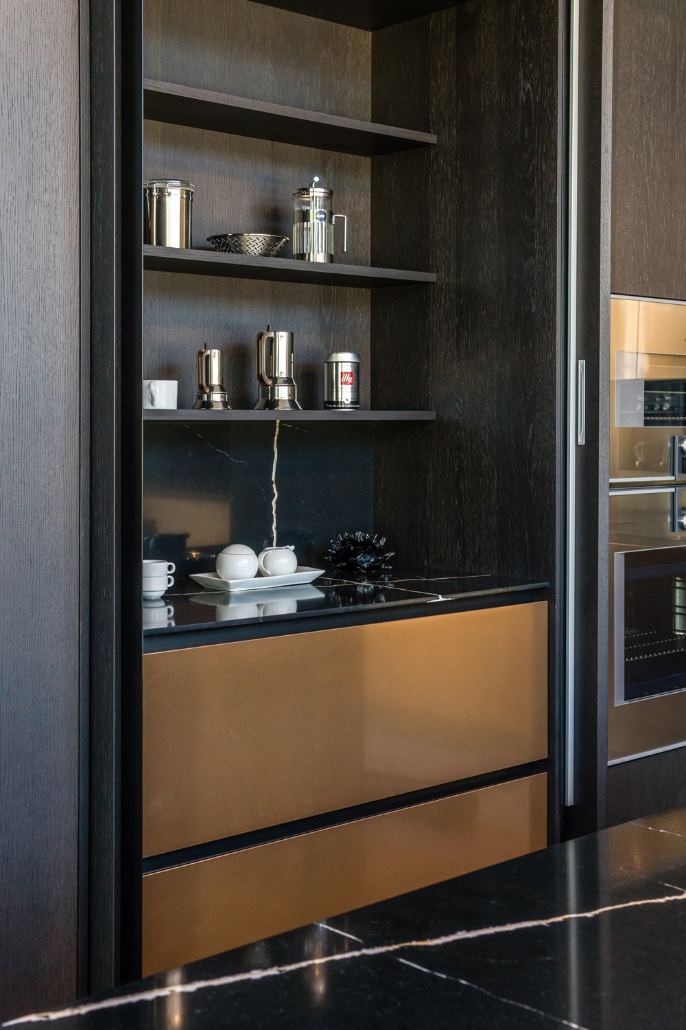 Detail of Los Angeles showroom kitchen in Station oak and Bronze Lux liquid metal. Wing system with pocket doors and a functional surface matching the kitchen countertops. Interior customizable with drawers, shelves, and accessories wall.