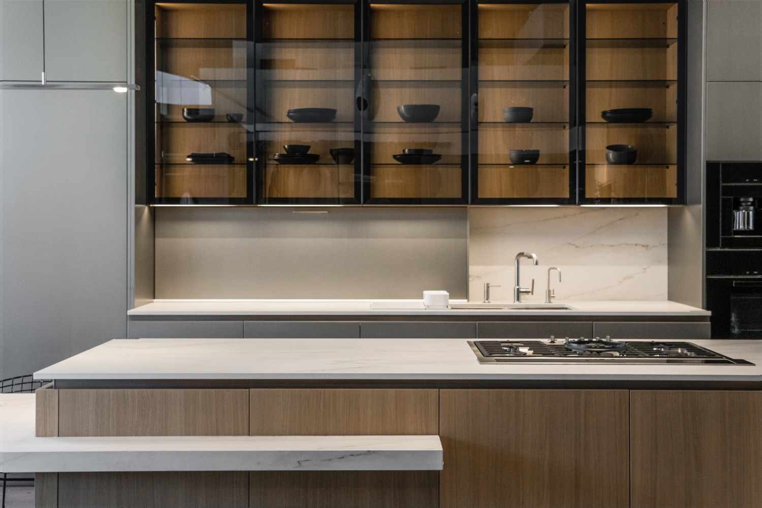 Framed glass cabinets with back panels in UV X-Duna oak wood (matching the island). Under the cabinets, the closed Mover system conceals an organized storage space.