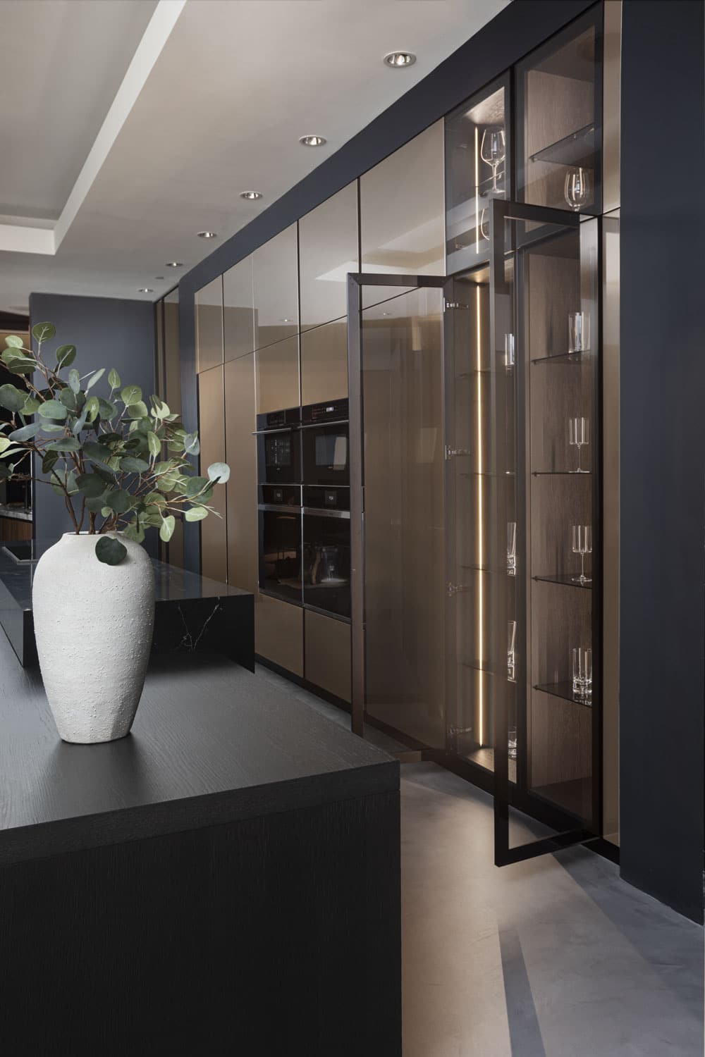 Tall cabinets with framed doors in smoked glass integrate within the pantry wall, creating an elegant display area. 