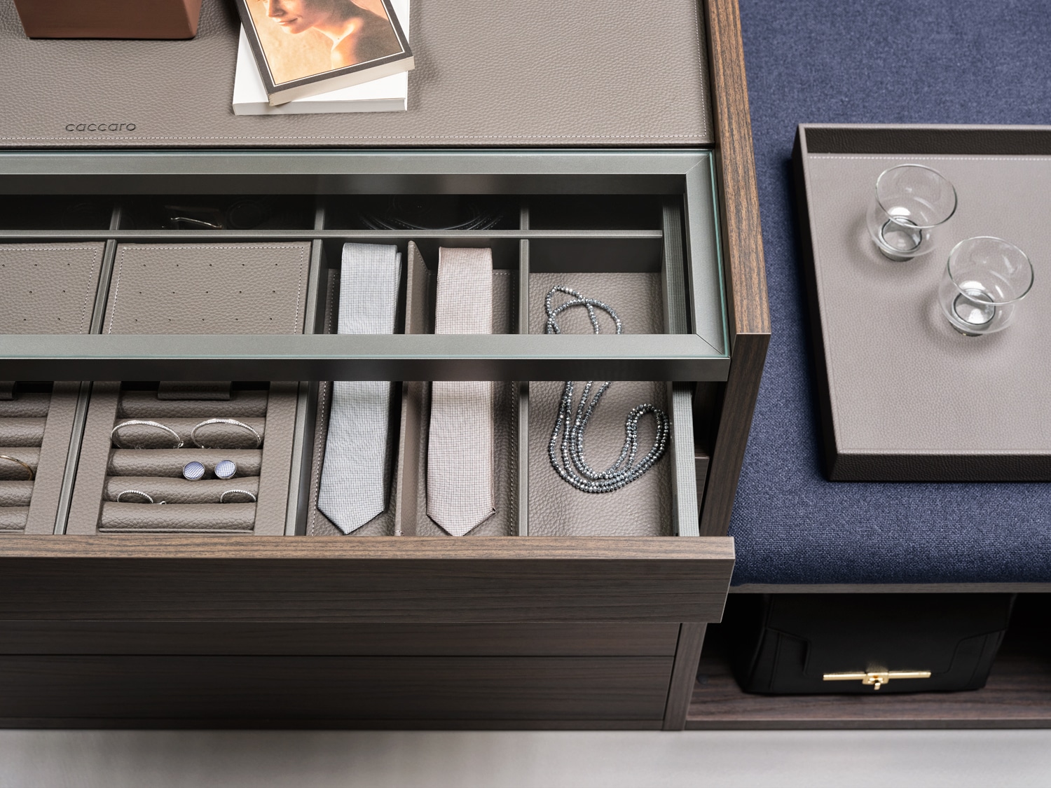 Detail of the top drawer of the central island with glass top and faux leather inserts to organize all your fashion accessories. The side bench turns the closet into a personal dressing room.