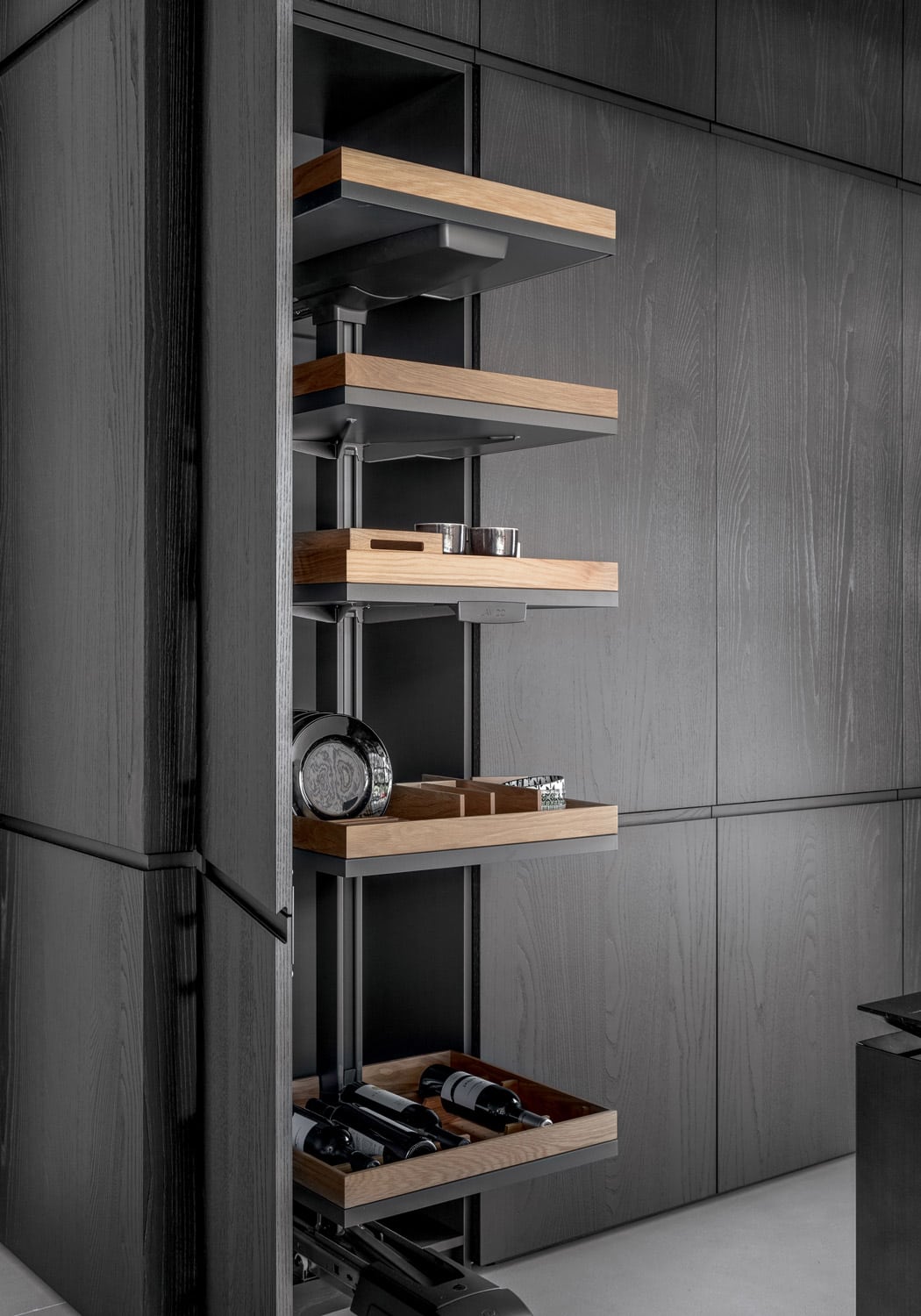 The side column features an extractable system of adjustable shelves, each with a customized tray in light wood to hold wine bottles, plates, containers, and other pantry items. 