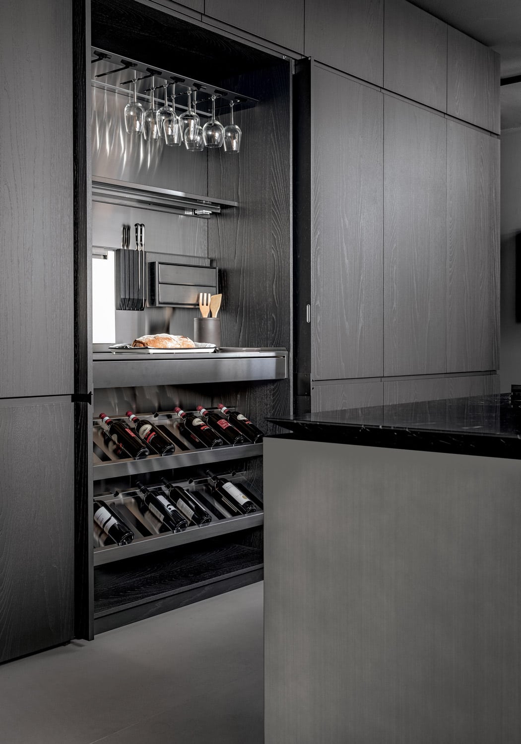 Multifunctional tall unit customized to house wine racks, drawers, glassware, and knives while also including a full pull-out stainless steel worktop to extend the usable surface area.