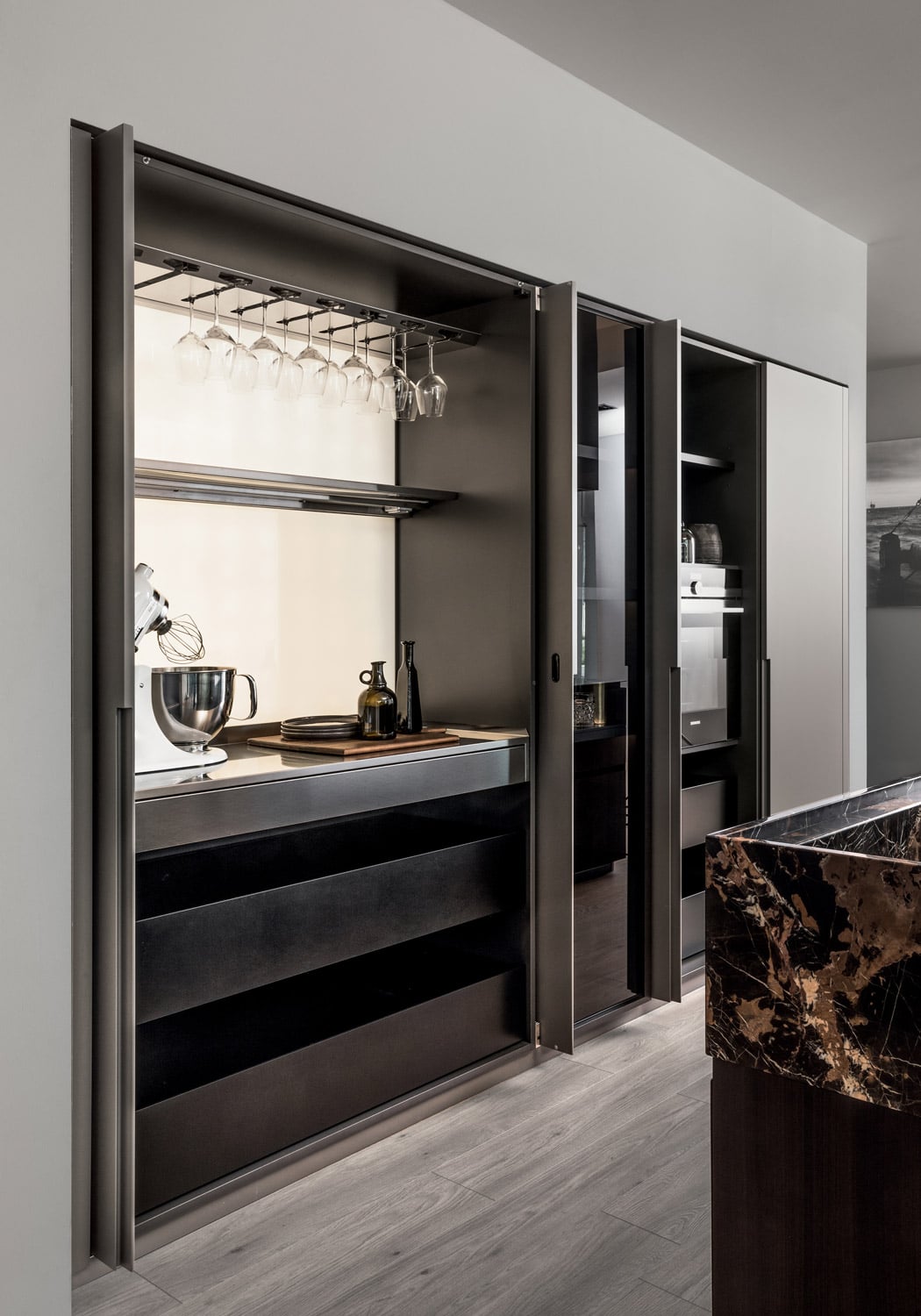 The units open with pocket doors which reveal customized storage and functional space including drawers, appliances, shelves, accessories racks, and worktops. 