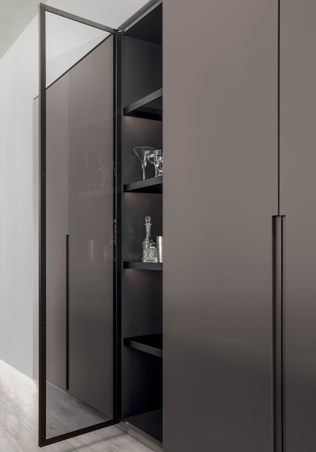 In the middle of the tall cabinets is a column with an aluminum-framed glass door. 
