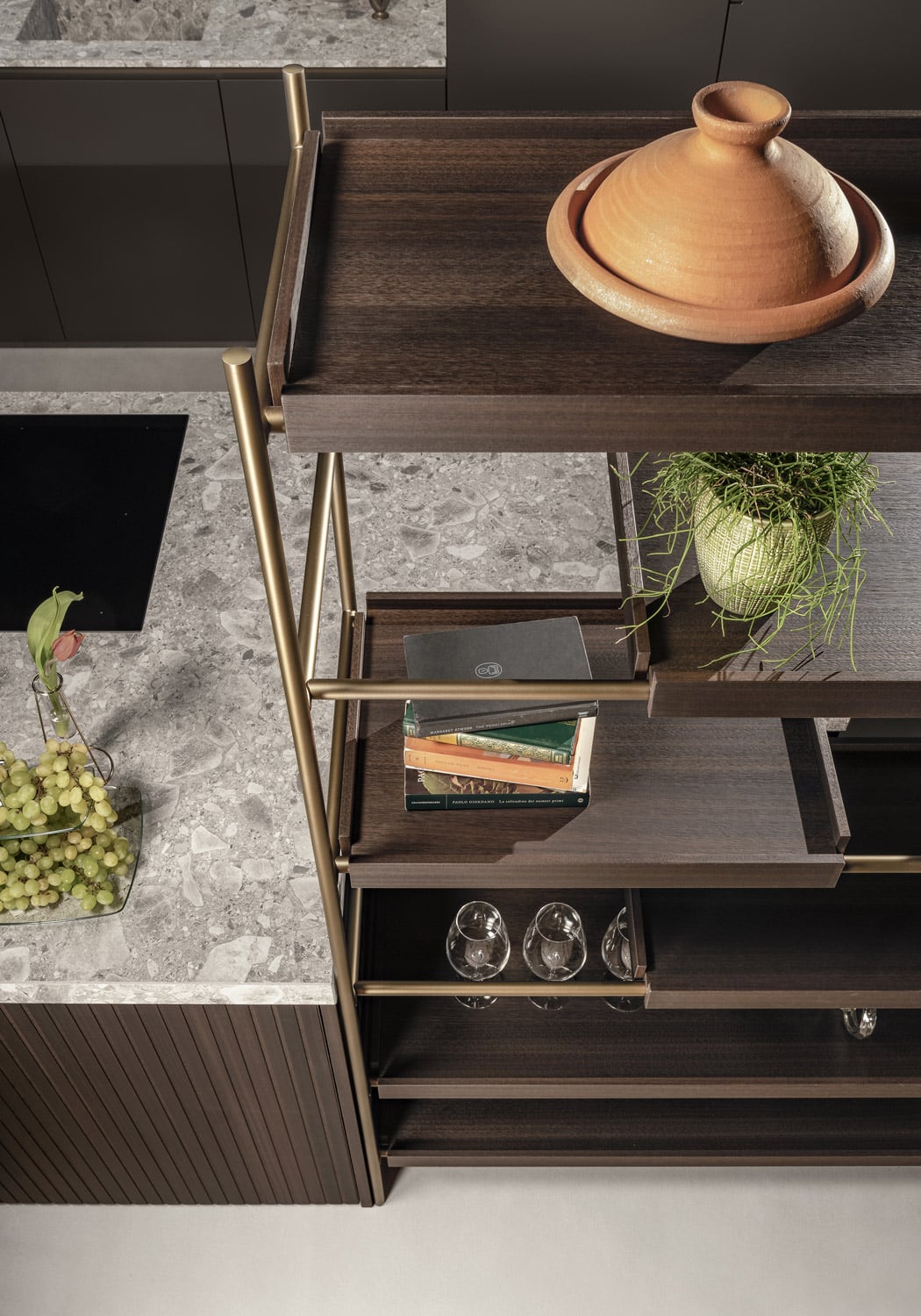 The bookcase system provides open storage, mirroring the Eucalyptus and Antique Brass finishes of the island. 