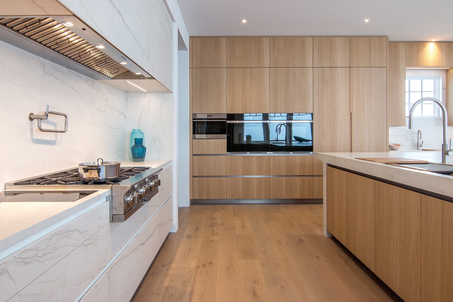 Monmouth | Rumson, New Jersey. Bespoke UNICA kitchen. The cooking unit features Neolith Mont Blanc on cabinets, counters, and backsplash. The rest of the cabinetry is in Bleached Light Oak. Titanium toe-kicks and channels. Designed by Maria Filimonova, designer of MandiCasa New York Flagship and the showroom team in collaboration with Anderson Campanella Architects. Bluestar range/hood. 