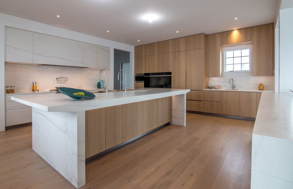 Large luxury kitchen with custom cabinets and island in Neolith Mont Blanc and light oak wood