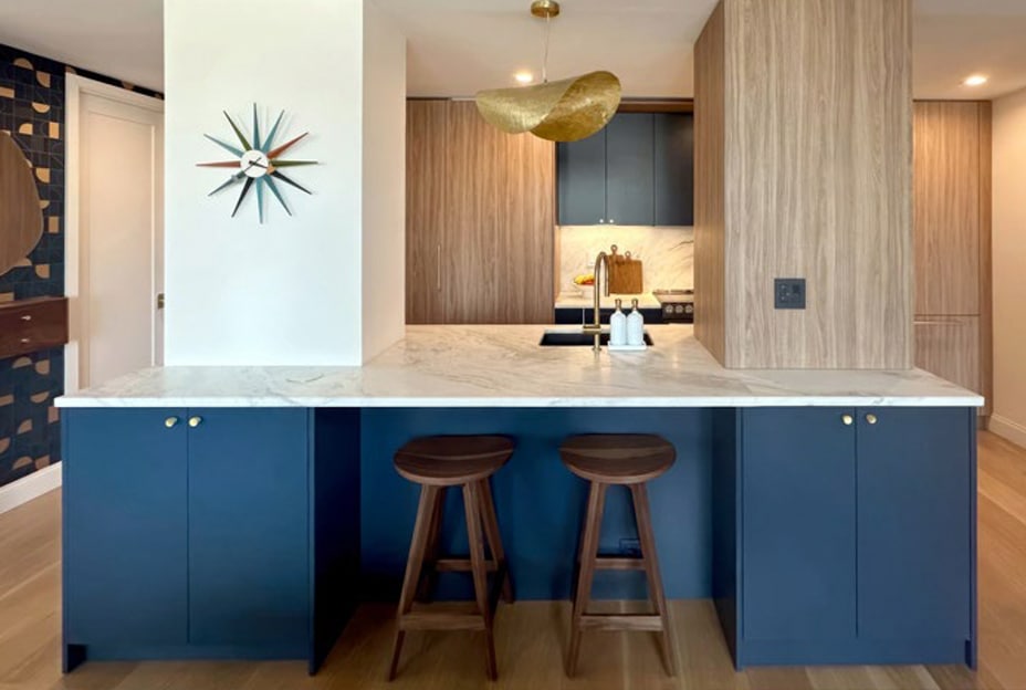 Modern kitchen with blue and wood cabinets, a marble countertop, and two wooden stools.
